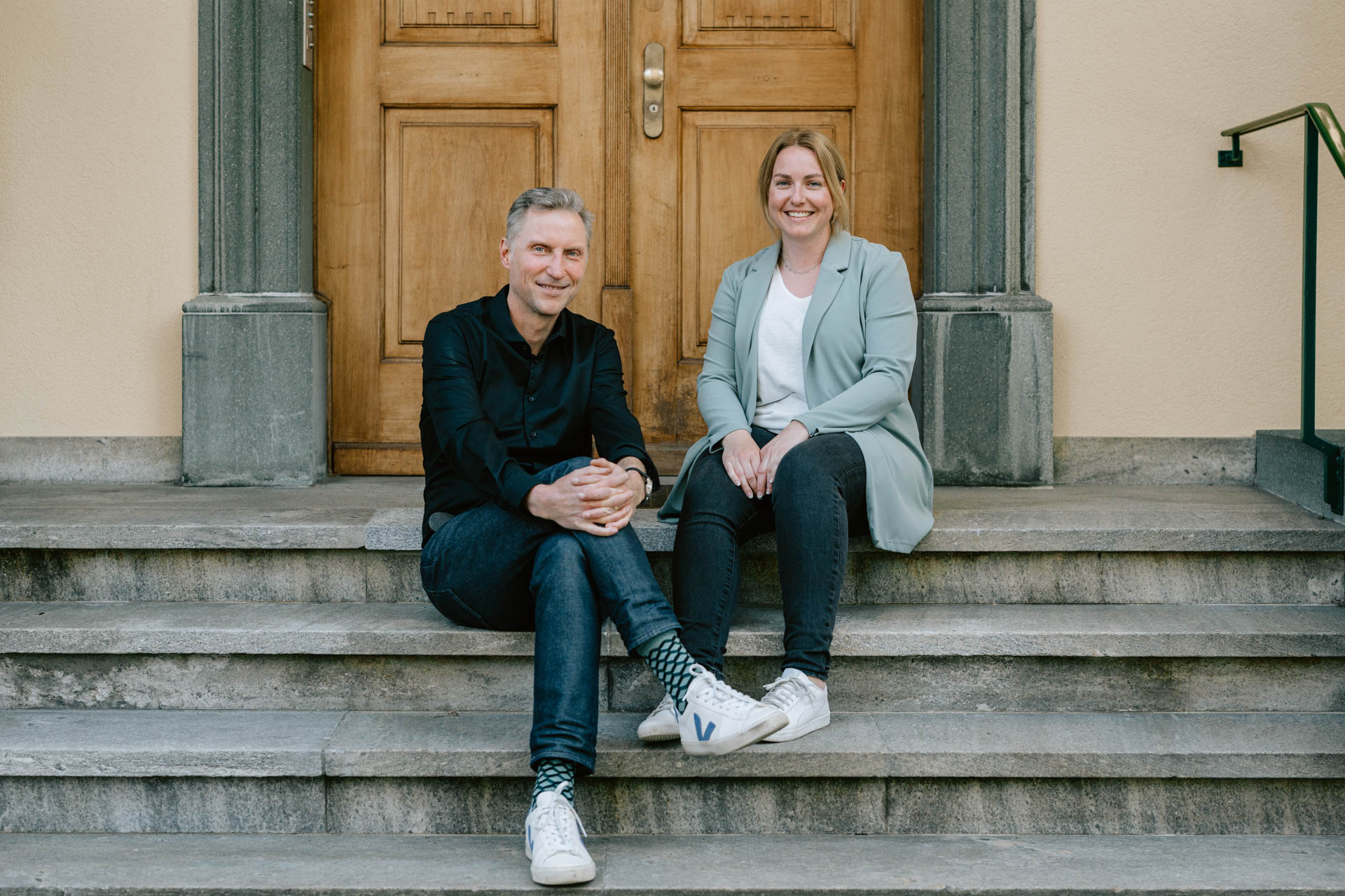 Stephan Schneiter und Micaela Baumgartner sitzen vor dem Eingang der Herzpraxis Sankt Gallen